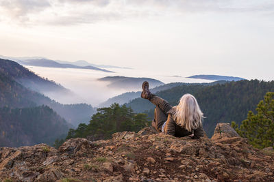 Woman hiker on a mountain top looking to low clouds and hills breaking through