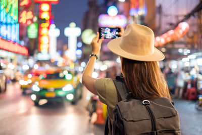 Rear view of woman standing by illuminated city street at night