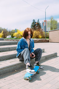 Young stylish woman wears sunglasses walks on the street with a skateboard