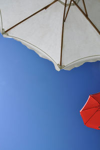 Low angle view of parasol against clear blue sky