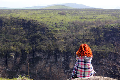 Girl with red hair sitting on the hill,landscape background