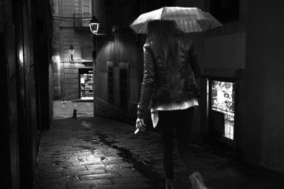 Rear view of woman walking on street during rainy season