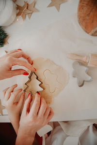 Hands of mom and baby cut out christmas cookies from the dough using metal molds on baking paper 