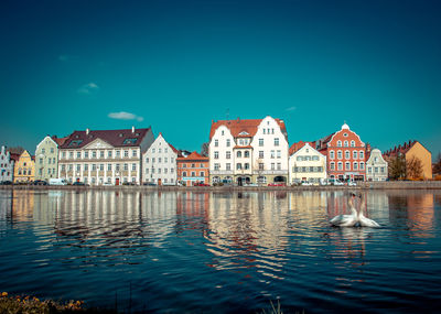 Buildings by river against blue sky