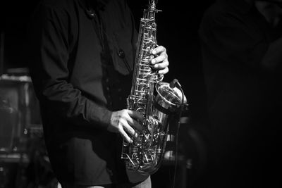 Midsection of man playing saxophone in darkroom