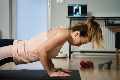 Woman in sports clothes does fitness cardio exercises at home, using laptop