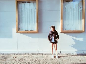 Full length of young woman standing against building on sunny day