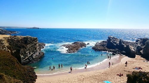 People on beach against clear blue sky