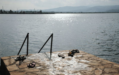 Footwear on jetty by lake against sky during sunny day