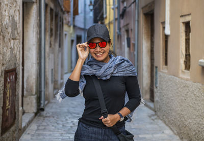 Woman wearing baseball cap and orange sunglasses in street alley