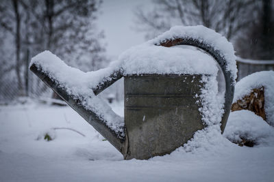 Watering can covered with snow on field