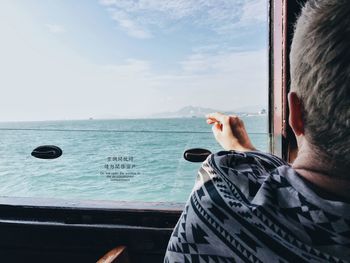 Rear view of man by window of ship in sea against sky