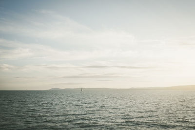 Sailboat appearing small on a quiet huge lake, with coast behind, at sunset.