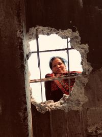 Portrait of smiling woman looking through damaged concrete wall
