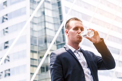Portrait of businessman drinking water while standing outdoors