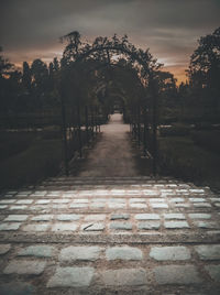 Empty footpath by trees against sky during sunset