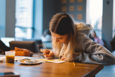 Pretty teenage girl draws a picture with poster paint.