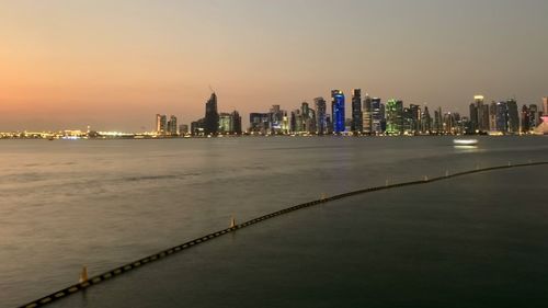 River by illuminated buildings against sky during sunset