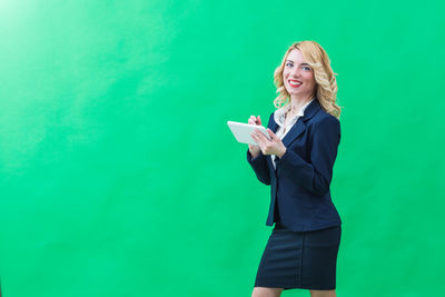 Portrait of happy businesswoman holding digital tablet against green wall