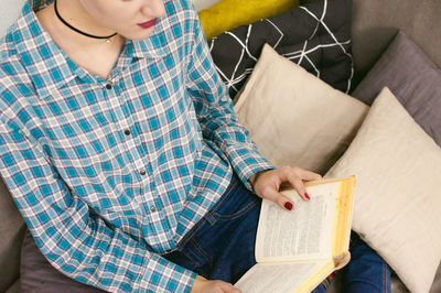 Midsection of young woman reading book while sitting on sofa at home