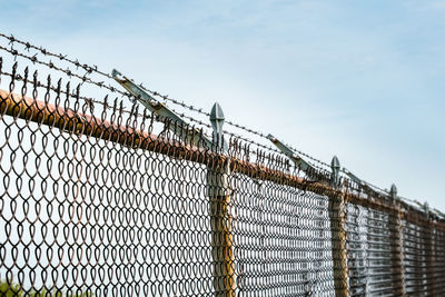 A long length of chain link fence topped with barbed wire set against cloudy sky - trapped
