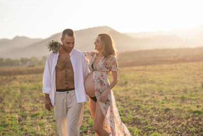 Pregnant woman standing with man against sky