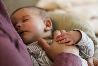 A baby boy sleeps in his mothers lap as she rest her hand on his belly