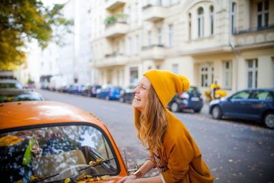 Side view of smiling young woman by car on street