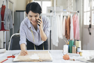 Cheerful fashion designer talking on phone while working at boutique