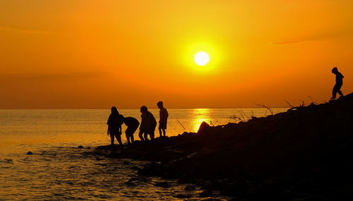 Silhouette people on beach against sky during sunset