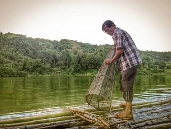 Side view of man standing by lake against clear sky