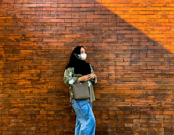 Young woman standing against brick wall