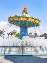 Chain swing ride over fountain against blue sky at amusement park