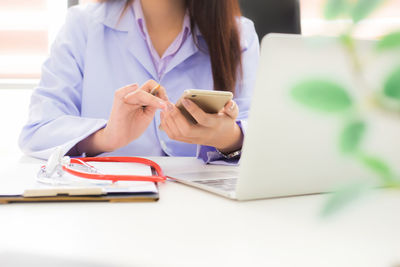 Midsection of woman using mobile phone while sitting on table