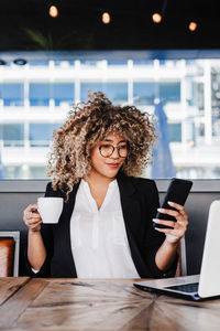 Young woman using mobile phone while sitting on table