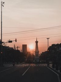 Street by silhouette buildings against sky during sunset