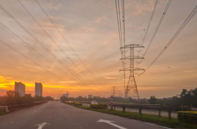 Electricity pylon by road against sky during sunset