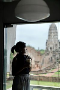 Side view of a young woman drinking glass window