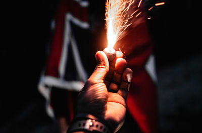 Cropped hand of person holding illuminated firecracker