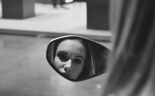 Young woman reflecting in side-view mirror of car