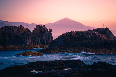 Rocks by sea against sky during sunset