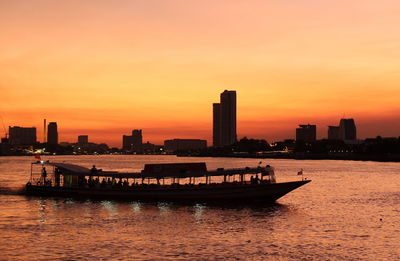 Sea by buildings against sky during sunset