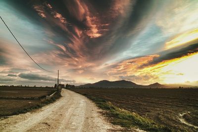 Road passing through field against cloudy sky