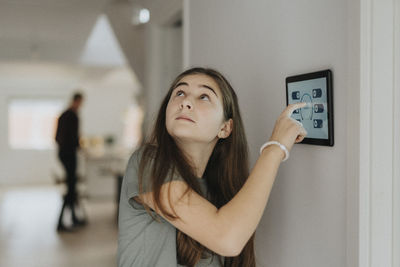 Pre-adolescent girl adjusting room temperature through digital tablet mounted on wall at home