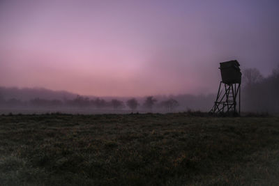 Silhouette tower on field against sky during sunset