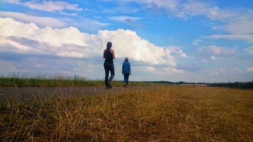 Rear view of couple walking on field against sky