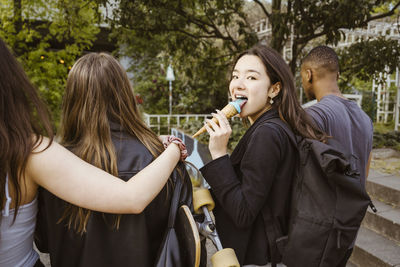 Young woman looking back while eating ice cream and walking with friends in city