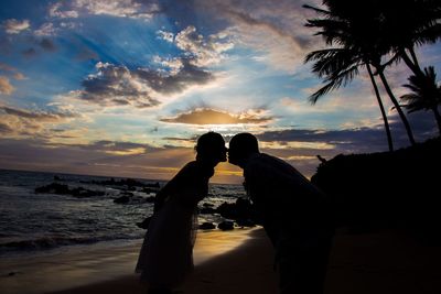 Silhouette couple kissing at beach against cloudy sky during sunset