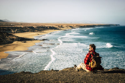 Man sitting on rock by sea against sky