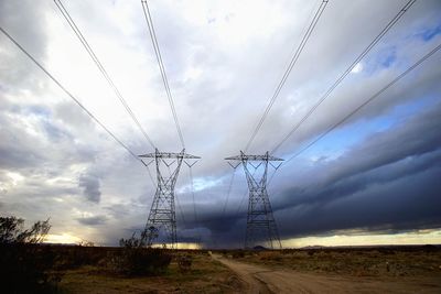 Low angle view of electricity pylon against cloudy sky